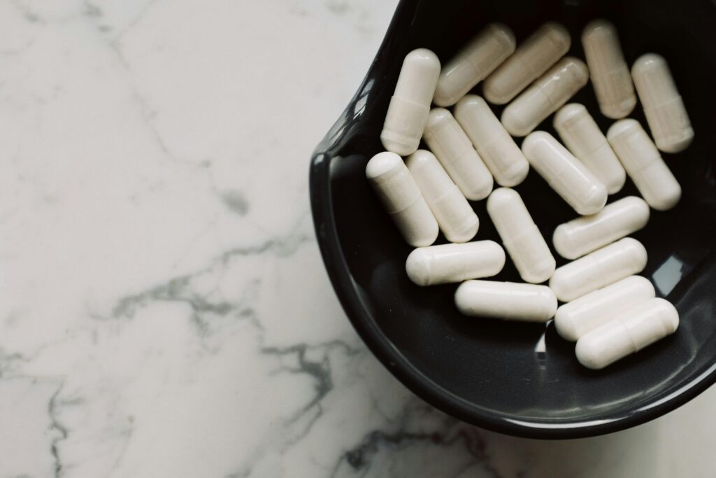 Close-up of white capsules in a black bowl on a marble surface, symbolizing healthcare and medication.