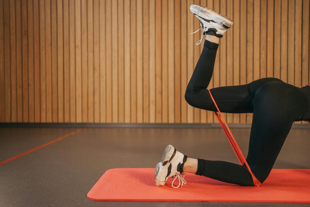 Woman in activewear working out indoors with resistance band on yoga mat, focusing on legs.