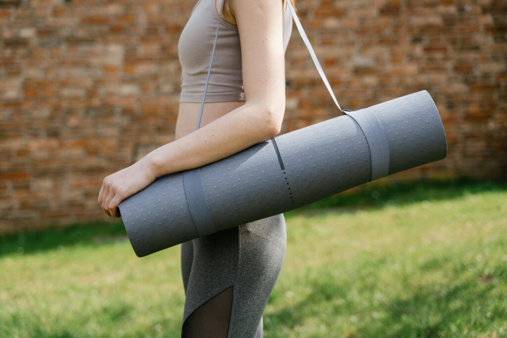 Woman holding a yoga mat outdoors, ready for exercise in the sun.