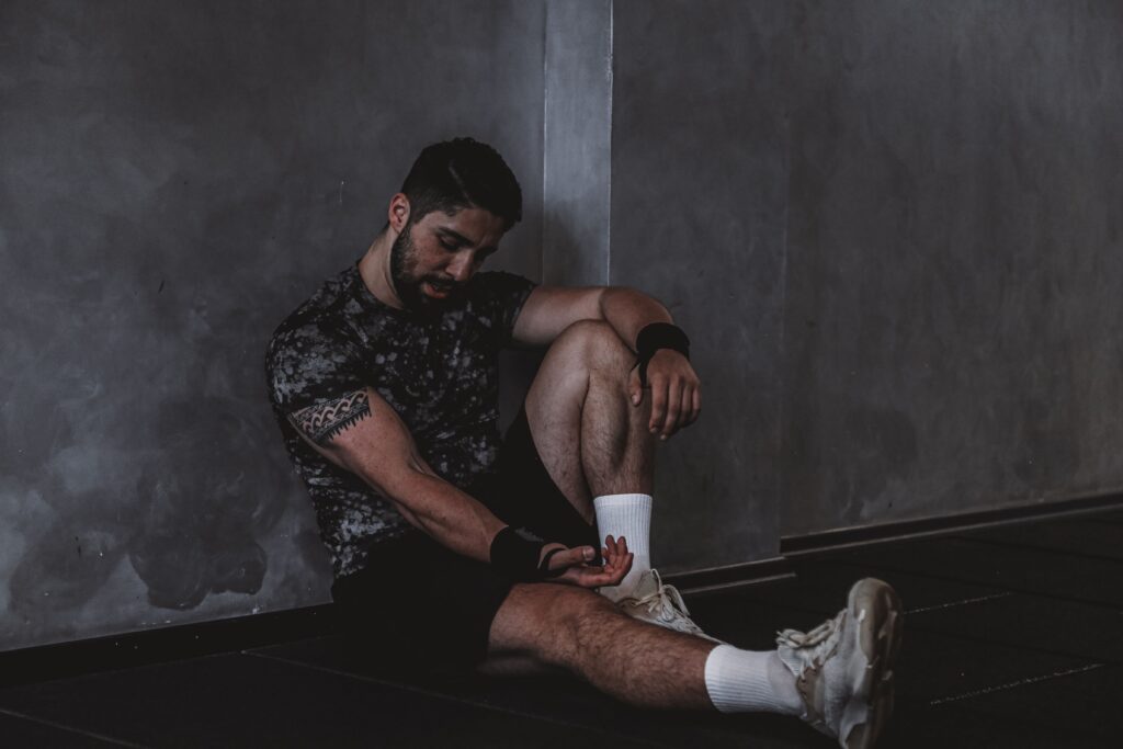 Recuperación Muscular: 7 Estrategias Clave para Recuperarte Más Rápido Después del Entrenamiento A muscular man in a gym environment taking a moment of rest, reflecting in a dark moody setting.