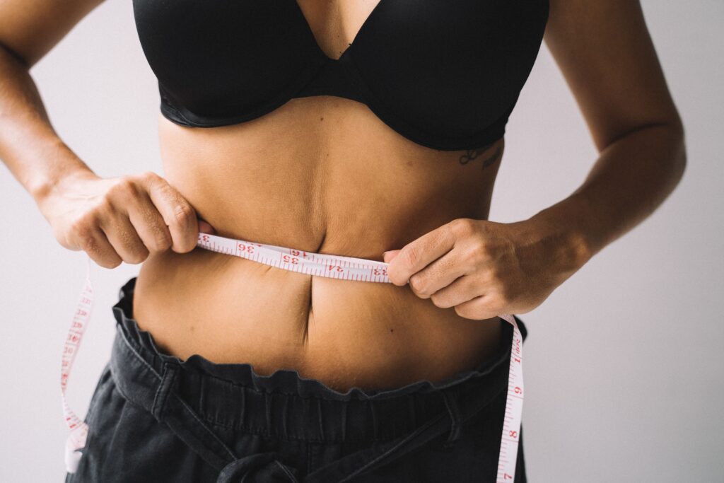 Cómo Perder Grasa Sin Perder Músculo: Guía Completa de Nutrición y Entrenamiento A woman measures her waist with a tape for fitness and weight loss results.