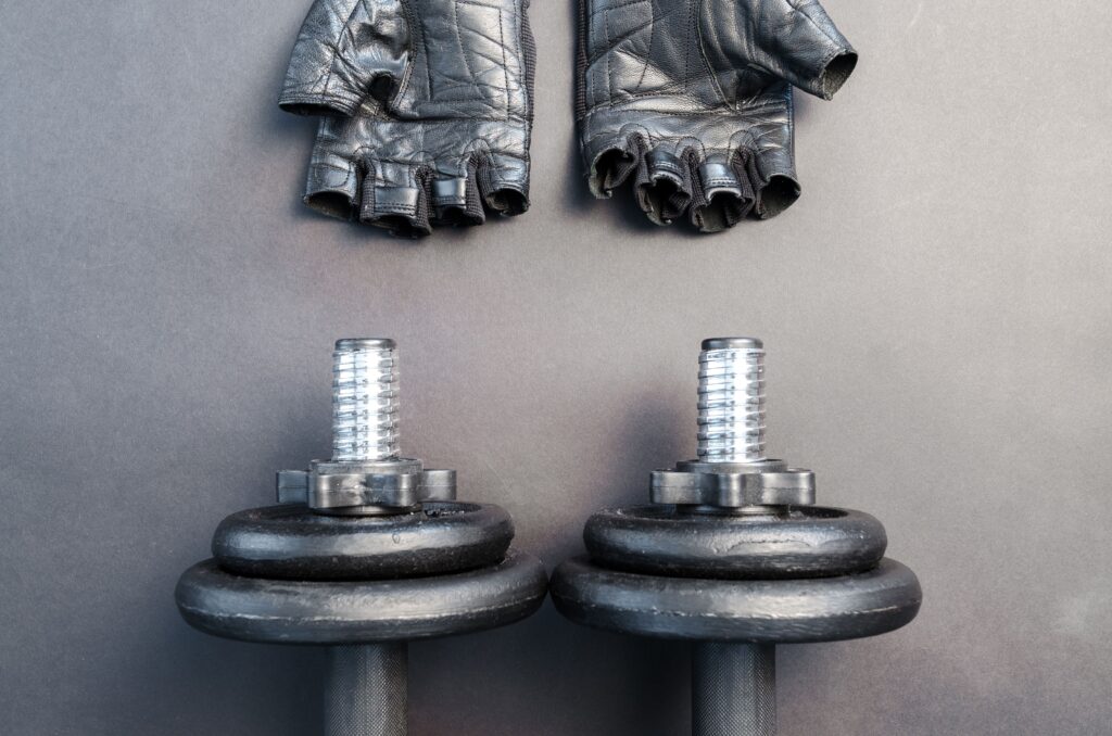 Mejores Guantes de Gimnasio 2026: Comparativa de las 6 Mejores Marcas para Entrenar Black dumbbells and leather gloves on a workout mat ready for fitness training.