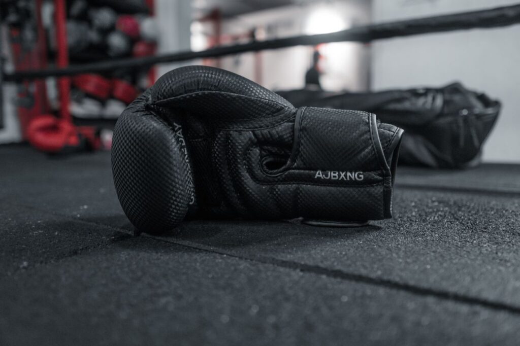 A close-up of a single black boxing glove lying on the gym floor, conveying a sense of resilience.