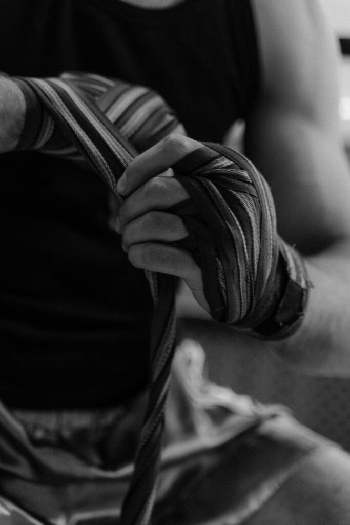 Mejores Vendas de Boxeo 2026: Comparativa RDX vs Venum vs Everlast vs Leone vs FIGHTR Grayscale photo of an athlete wrapping hands, focusing on wrapped fingers and forearm.