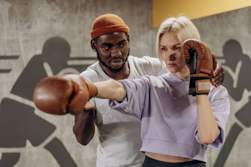 Rutina de Boxeo en Casa para Principiantes: 45 Minutos sin Equipamiento A trainer guides a boxer's punching technique during an indoor gym session.