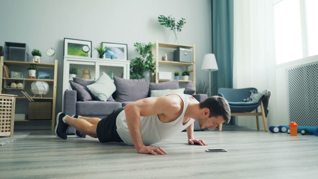 Entrenamiento de Fuerza en Casa sin Material: Rutina Completa de Calistenia para Todo el Cuerpo A muscular man performing push-ups in a modern living room, showcasing home fitness.