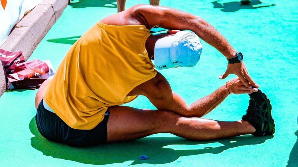 Estiramientos y Movilidad: Rutina de 15 Minutos para Mejorar tu Flexibilidad Athletic man stretches on a vibrant outdoor sports court, focusing on flexibility and fitness.
