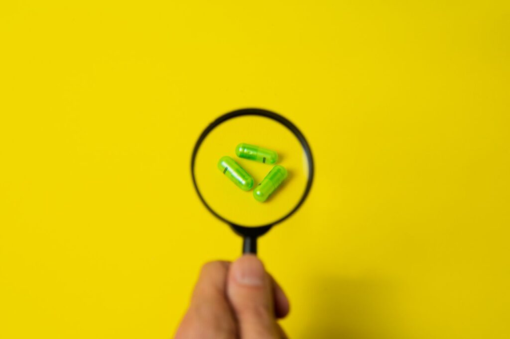 Colágeno para Deportistas: Beneficios, Tipos y Cómo Tomarlo Top view of crop unrecognizable person holding magnifier over green pills placed on bright yellow surface in studio