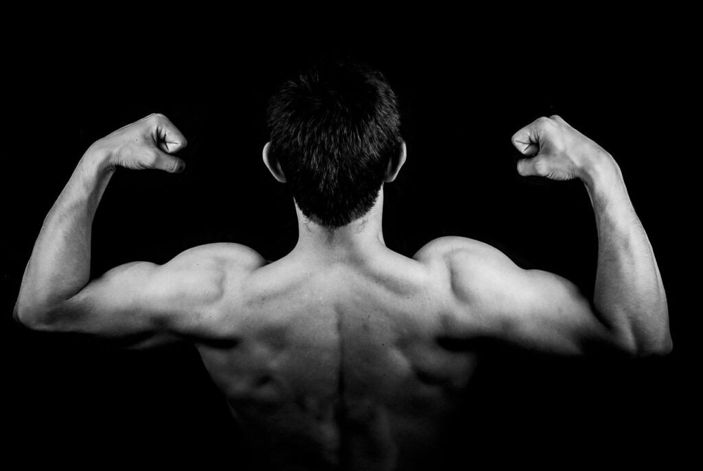 Cómo Aumentar la Testosterona de Forma Natural: 10 Estrategias Basadas en la Ciencia Black and white photo of a muscular man flexing arms against a dark background.